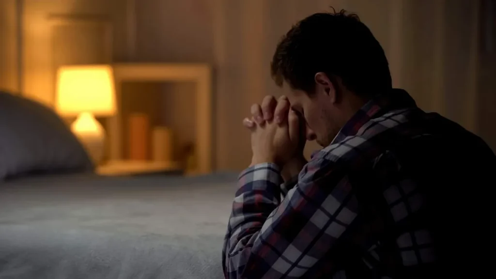 Imagem homem rezando ao pe da cama a noite do artigo Rezar de dia ou à noite? Qual o melhor horário?